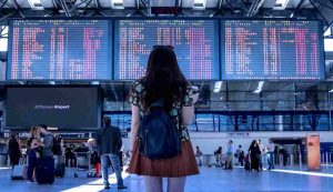 turista in aeroporto davanti al tabellone delle partenze